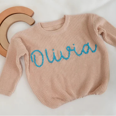 Beige sweater with 'Olivia' embroidered in blue on a white background
