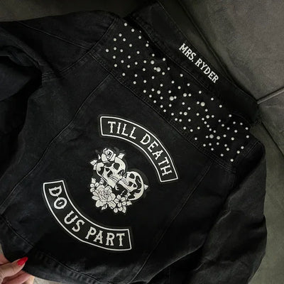 Black jacket with studded details and embroidered text on a dark surface