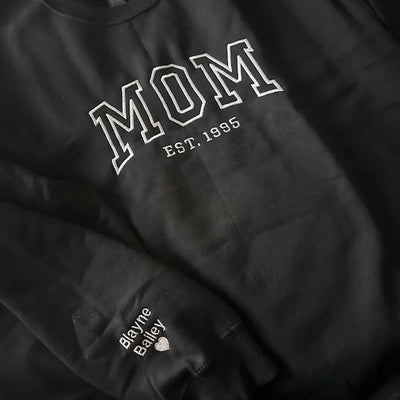 Black sweatshirt with 'MOM EST. 1995' text on a dark background