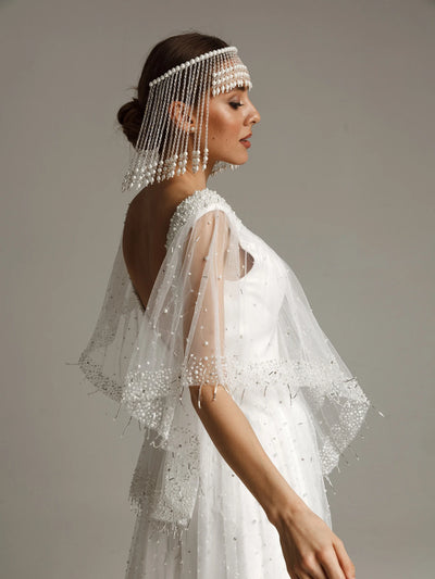 Woman wearing a white beaded headpiece and dress against a neutral background