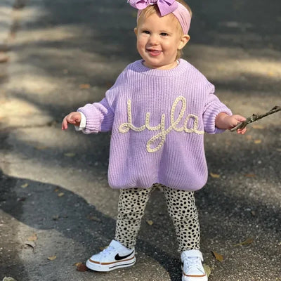 Child wearing a purple sweater with 'Lyla' on it, standing outdoors.