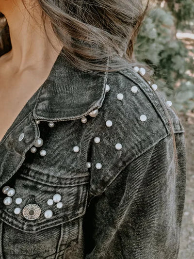 Denim jacket with pearl embellishments worn by a person outdoors.
