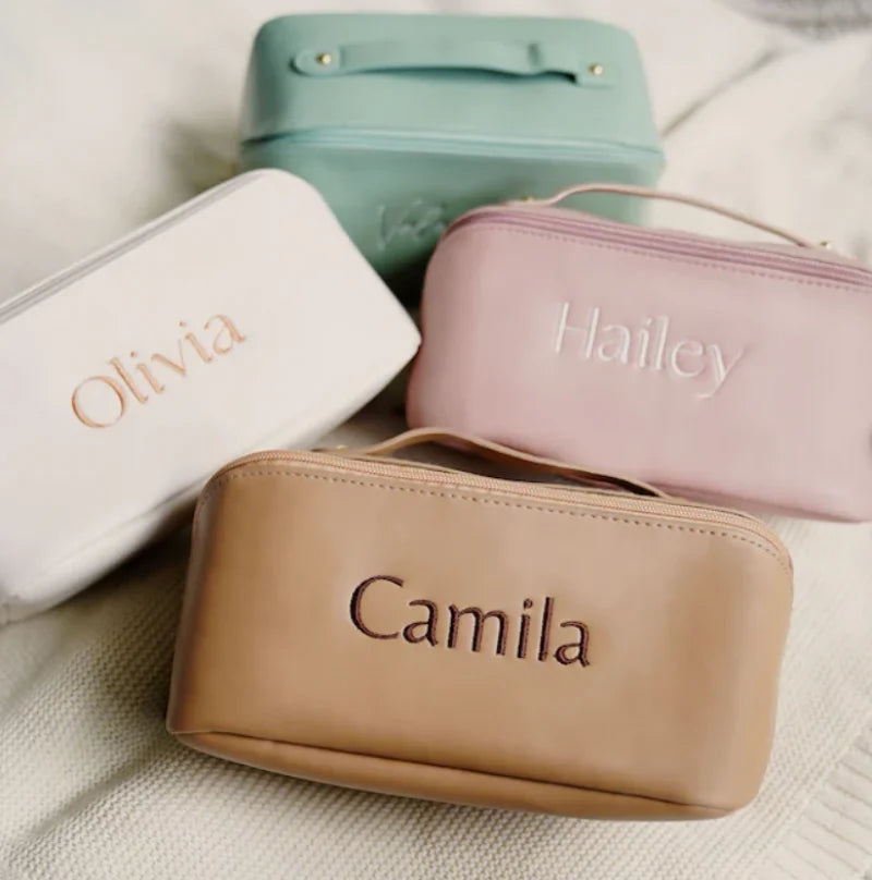 Four personalized cosmetic bags in different colors with names engraved on them.