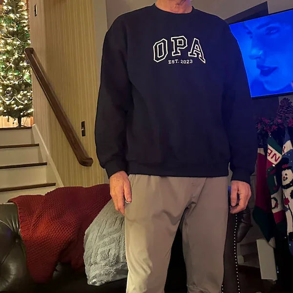 Person wearing a navy blue sweatshirt with 'OPA EST. 2023' text in a home setting.