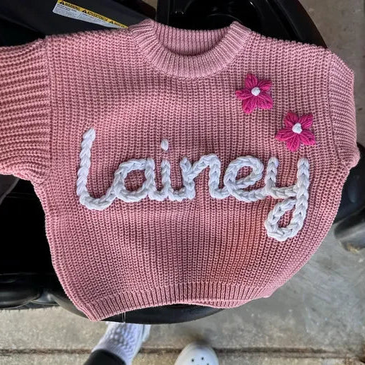 Pink sweater with 'Lainey' and floral designs on a person sitting in a vehicle.