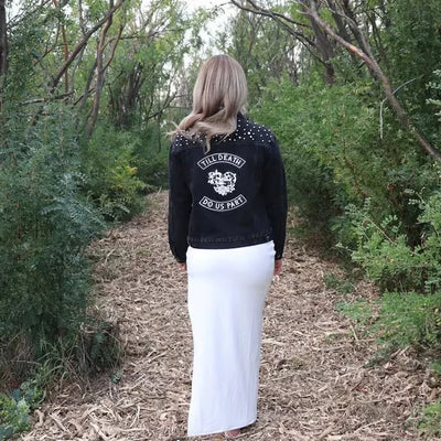 Person wearing a black jacket with text and graphics, walking through a forest path.