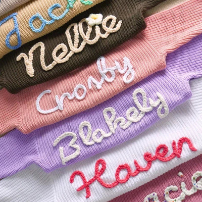 Stack of knit sweaters with embroidered names in various colors.