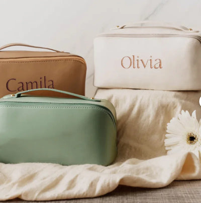 Three cosmetic bags with 'Camila', 'Olivia', and another name partially visible on a textured surface.