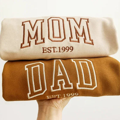 Two sweatshirts stacked on top of each other with 'Mom' and 'Dad' text.